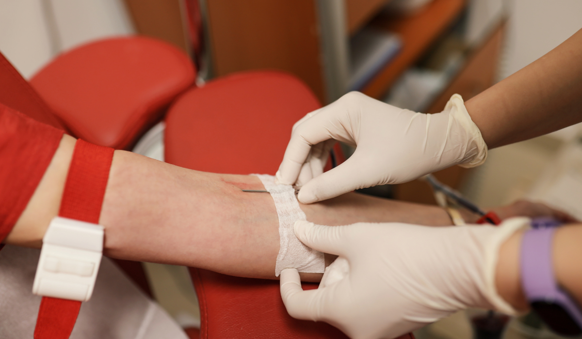 Phlebotomist taping a cannula to a donor's arm during collection